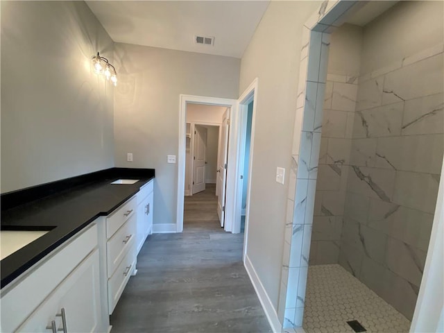 bathroom featuring hardwood / wood-style flooring, tiled shower, and vanity