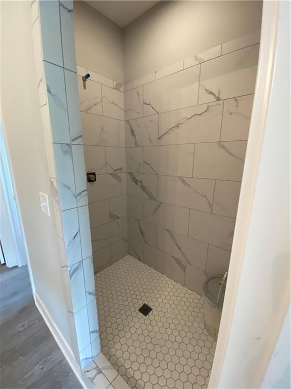 bathroom with wood-type flooring, toilet, and tiled shower