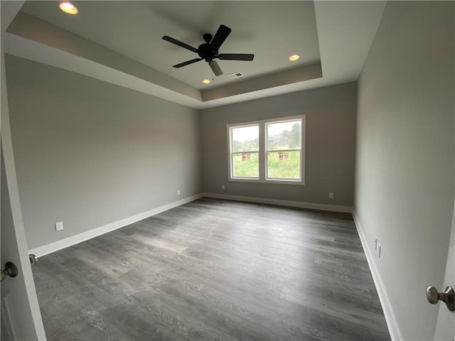 unfurnished room with ceiling fan, a tray ceiling, and dark wood-type flooring