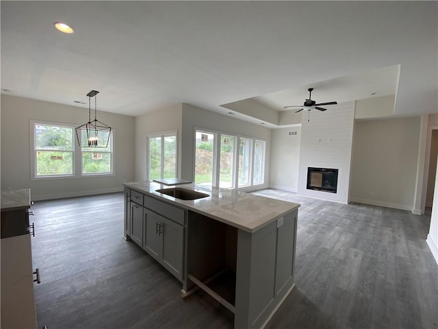 kitchen featuring a center island with sink, decorative light fixtures, dark wood-type flooring, gray cabinets, and light stone countertops