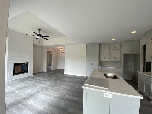 kitchen featuring ceiling fan, sink, gray cabinetry, a kitchen island with sink, and dark hardwood / wood-style flooring