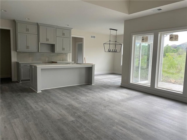 kitchen featuring an inviting chandelier, gray cabinetry, hardwood / wood-style floors, a center island with sink, and hanging light fixtures