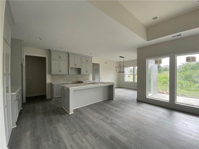 kitchen featuring a kitchen island with sink, gray cabinetry, pendant lighting, a notable chandelier, and dark hardwood / wood-style floors