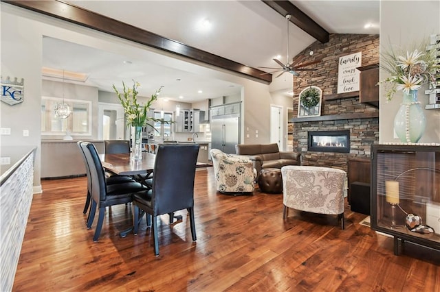 dining space with lofted ceiling with beams, a fireplace, dark hardwood / wood-style floors, and ceiling fan with notable chandelier