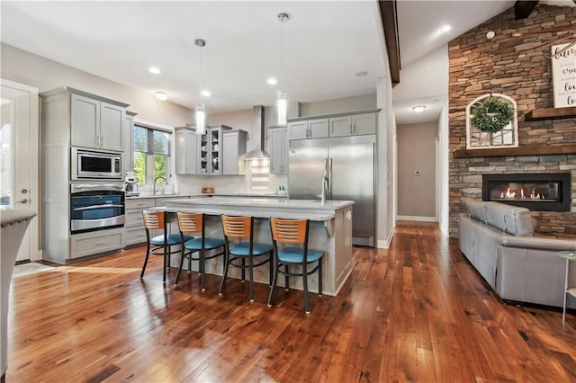 kitchen with built in appliances, wall chimney exhaust hood, dark wood-type flooring, and hanging light fixtures