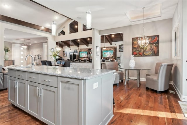 kitchen featuring a center island with sink, sink, dark wood-type flooring, and hanging light fixtures