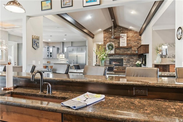 kitchen with sink, a stone fireplace, wall chimney exhaust hood, decorative light fixtures, and built in refrigerator