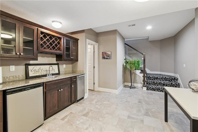 kitchen with dark brown cabinetry, dishwasher, light stone counters, and sink