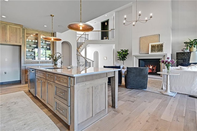 kitchen featuring light wood-type flooring, hanging light fixtures, a high ceiling, and an island with sink