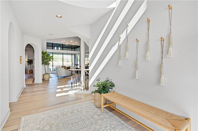 hallway with light hardwood / wood-style floors, vaulted ceiling, and a notable chandelier