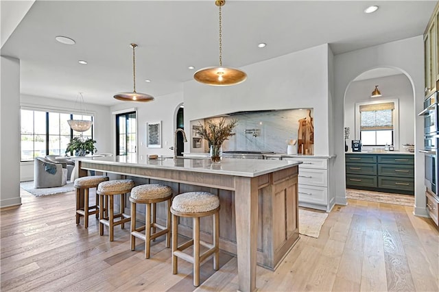 kitchen with white cabinets, plenty of natural light, a kitchen island with sink, and hanging light fixtures