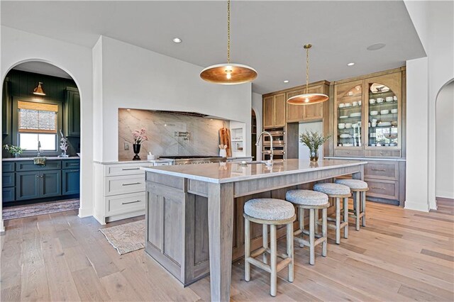 kitchen with tasteful backsplash, a kitchen island with sink, pendant lighting, light hardwood / wood-style flooring, and a breakfast bar area