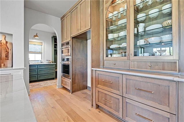 interior space with light stone counters, double oven, and light hardwood / wood-style flooring