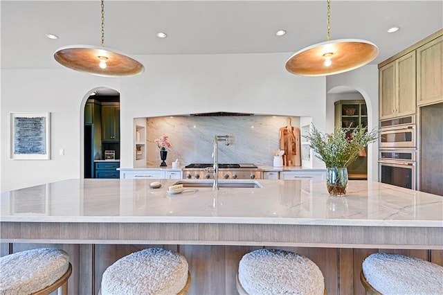 kitchen featuring a large island with sink, light stone counters, stainless steel double oven, and pendant lighting