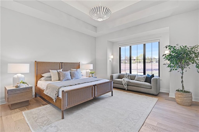 bedroom featuring a chandelier, a tray ceiling, and light hardwood / wood-style flooring