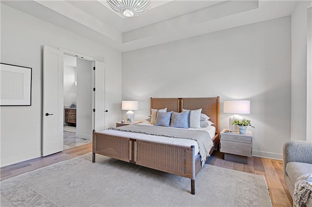 bedroom featuring hardwood / wood-style floors, a tray ceiling, and a chandelier