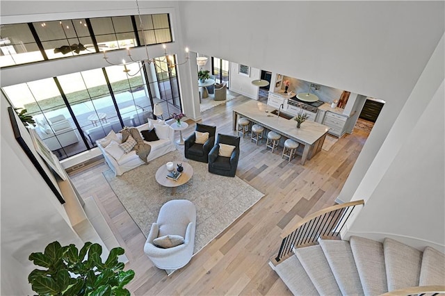 living room featuring light hardwood / wood-style flooring, a towering ceiling, an inviting chandelier, and sink