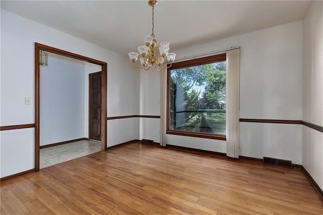 empty room featuring a notable chandelier and light wood-type flooring