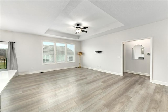 unfurnished living room with a raised ceiling, ceiling fan, and light hardwood / wood-style flooring