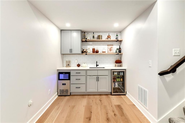 bar featuring sink, wine cooler, light hardwood / wood-style flooring, backsplash, and gray cabinets