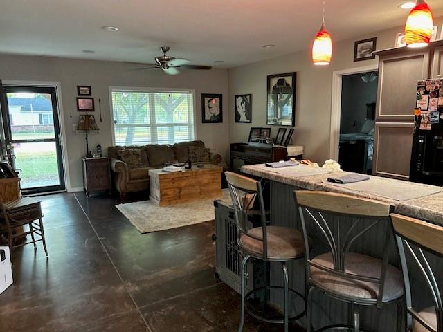 kitchen with black fridge, ceiling fan, hanging light fixtures, and a breakfast bar area