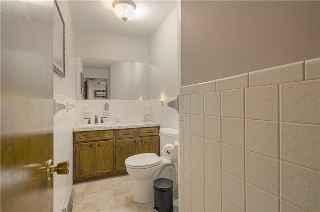 bathroom featuring tile walls, vanity, a textured ceiling, and toilet