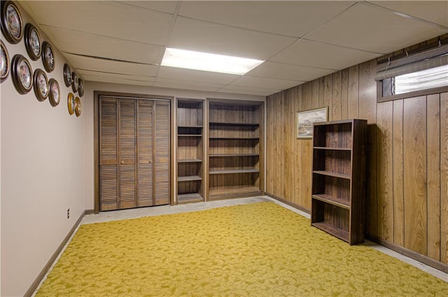 basement with a drop ceiling, light colored carpet, and wooden walls