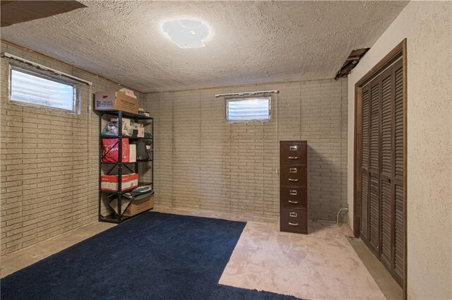 basement featuring a textured ceiling, brick wall, and plenty of natural light