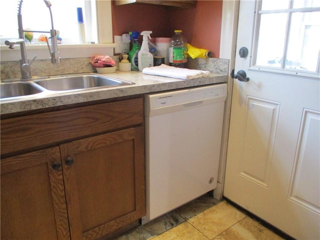 kitchen featuring brown cabinetry, dishwasher, light countertops, a sink, and light tile patterned flooring