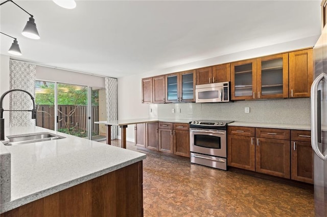 kitchen with brown cabinets, stainless steel appliances, hanging light fixtures, glass insert cabinets, and a sink