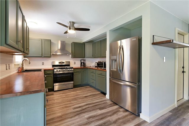 kitchen featuring ceiling fan, hardwood / wood-style floors, stainless steel appliances, wall chimney exhaust hood, and sink