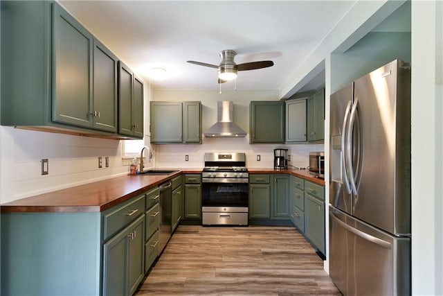 kitchen featuring sink, butcher block countertops, light hardwood / wood-style flooring, wall chimney range hood, and appliances with stainless steel finishes