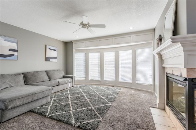 living room with a textured ceiling, a tiled fireplace, light carpet, and ceiling fan