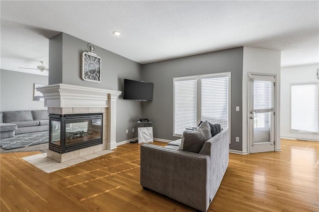 living room with hardwood / wood-style floors, a tile fireplace, ceiling fan, and a textured ceiling