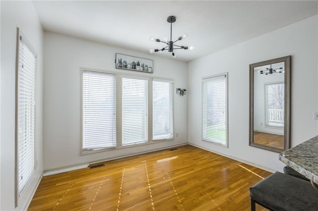 unfurnished dining area with an inviting chandelier and hardwood / wood-style flooring