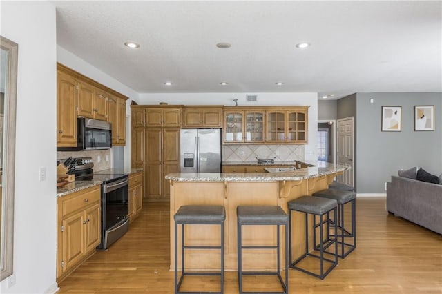 kitchen with a kitchen bar, light hardwood / wood-style flooring, backsplash, light stone countertops, and appliances with stainless steel finishes