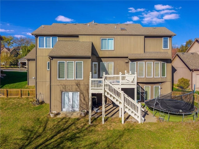 rear view of property with a wooden deck, a yard, and a trampoline