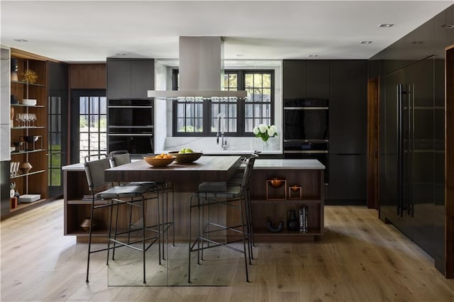 kitchen featuring double oven, a center island, light wood-type flooring, and a breakfast bar area