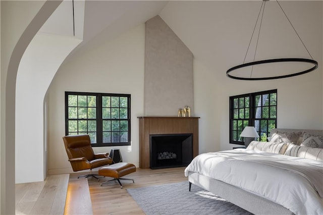 bedroom with a large fireplace, light hardwood / wood-style flooring, high vaulted ceiling, and multiple windows