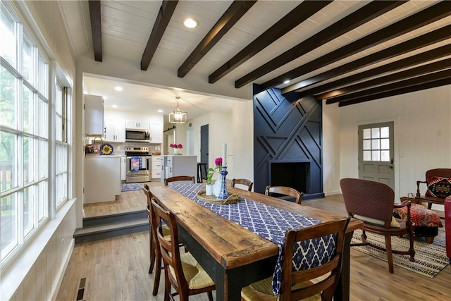 dining area featuring light wood-type flooring and beamed ceiling