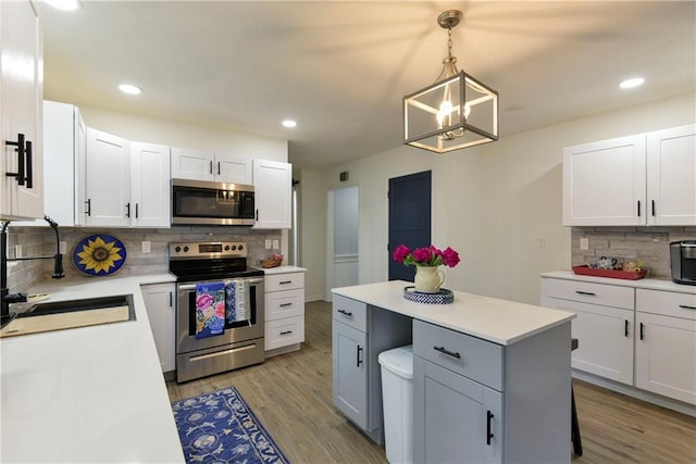 kitchen featuring stainless steel appliances, sink, hanging light fixtures, white cabinetry, and light hardwood / wood-style flooring