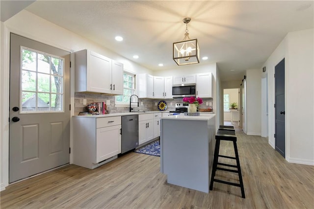 kitchen with decorative light fixtures, light hardwood / wood-style flooring, white cabinetry, stainless steel appliances, and a center island