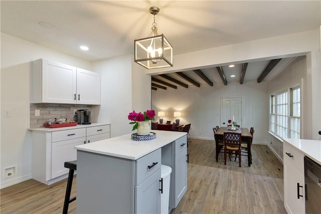 kitchen featuring hanging light fixtures, beam ceiling, stainless steel dishwasher, light hardwood / wood-style flooring, and white cabinetry