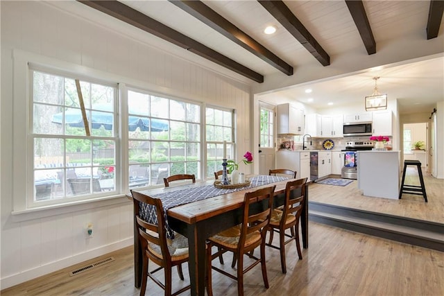 dining space with beam ceiling, light hardwood / wood-style flooring, and a wealth of natural light