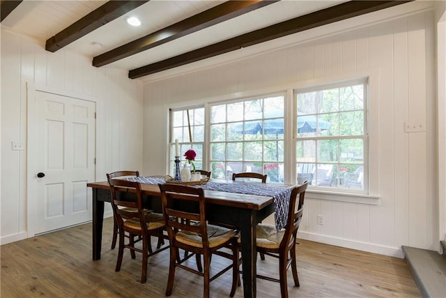 dining area featuring wood-type flooring, beam ceiling, and wooden walls