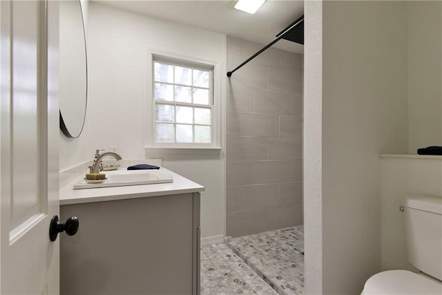 bathroom featuring vanity, tiled shower, and toilet