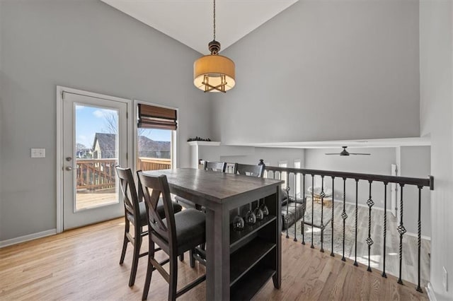 dining space with ceiling fan, high vaulted ceiling, and light hardwood / wood-style flooring