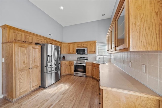 kitchen with sink, light wood-type flooring, backsplash, stainless steel appliances, and high vaulted ceiling