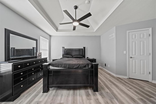 bedroom with a raised ceiling, light wood-type flooring, and ceiling fan