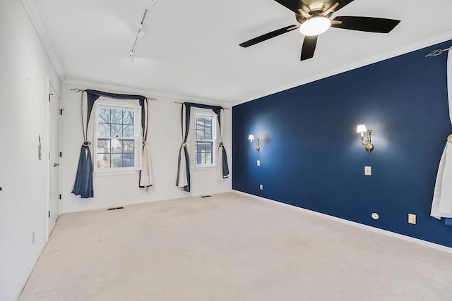 carpeted spare room with visible vents, ornamental molding, track lighting, baseboards, and ceiling fan